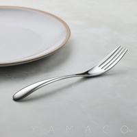 一個金屬叉子放在灰色大理石紋的桌面上，旁邊有一個白色的盤子，盤子的邊緣有淺棕色的裝飾。