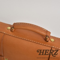 職人手作皮革傳統歐風三用學生包，展示包款的皮革手把與金屬卯釘細節，淺棕色皮革搭配米白色車線，質感細緻。