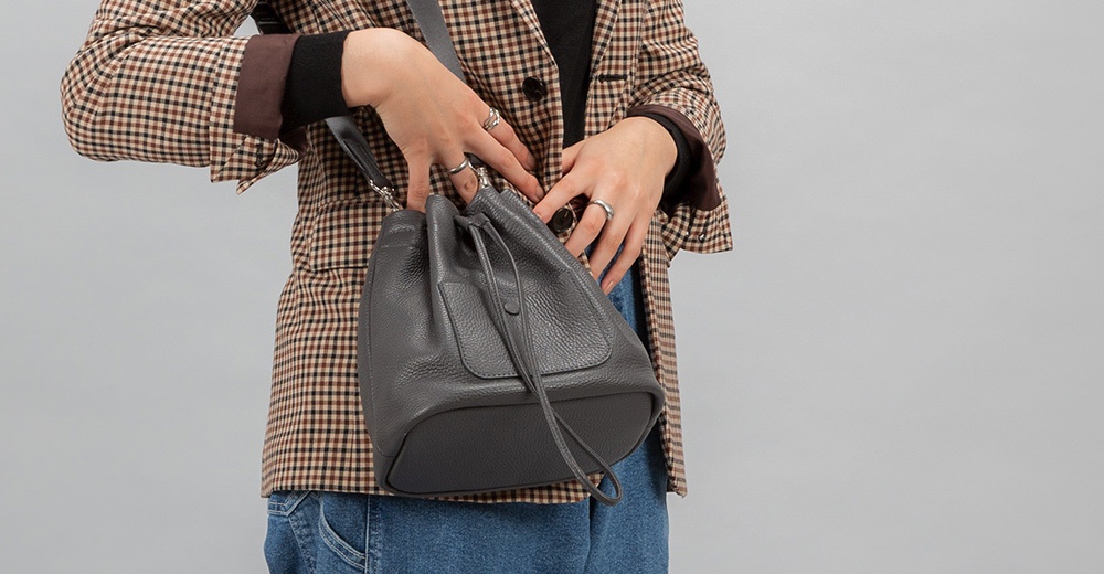 itten-itten BOLLA 義大利皮革束口水桶包，以灰色調呈現，配搭格紋外套和牛仔褲，展現時尚休閒風格。