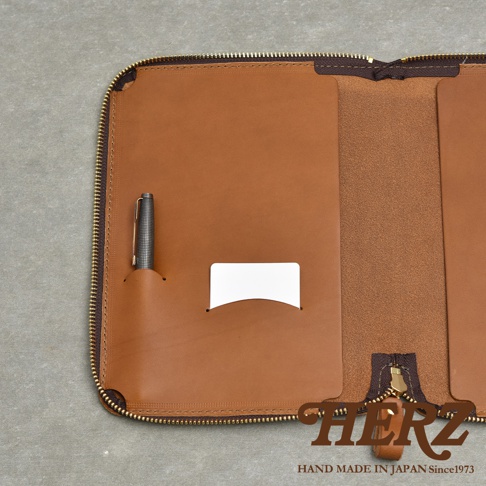 皮革記事本收納包，內有筆插和卡片夾，黃銅拉鍊，背面有皮革品牌標誌。