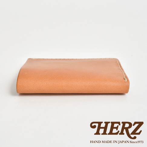 日本HERZ品牌手工皮革二折式薄型卡片鈔票夾，簡約裸色皮革，背面有手工縫線細節，下方印有HERZ品牌標誌與MADE IN JAPAN Since1973字樣