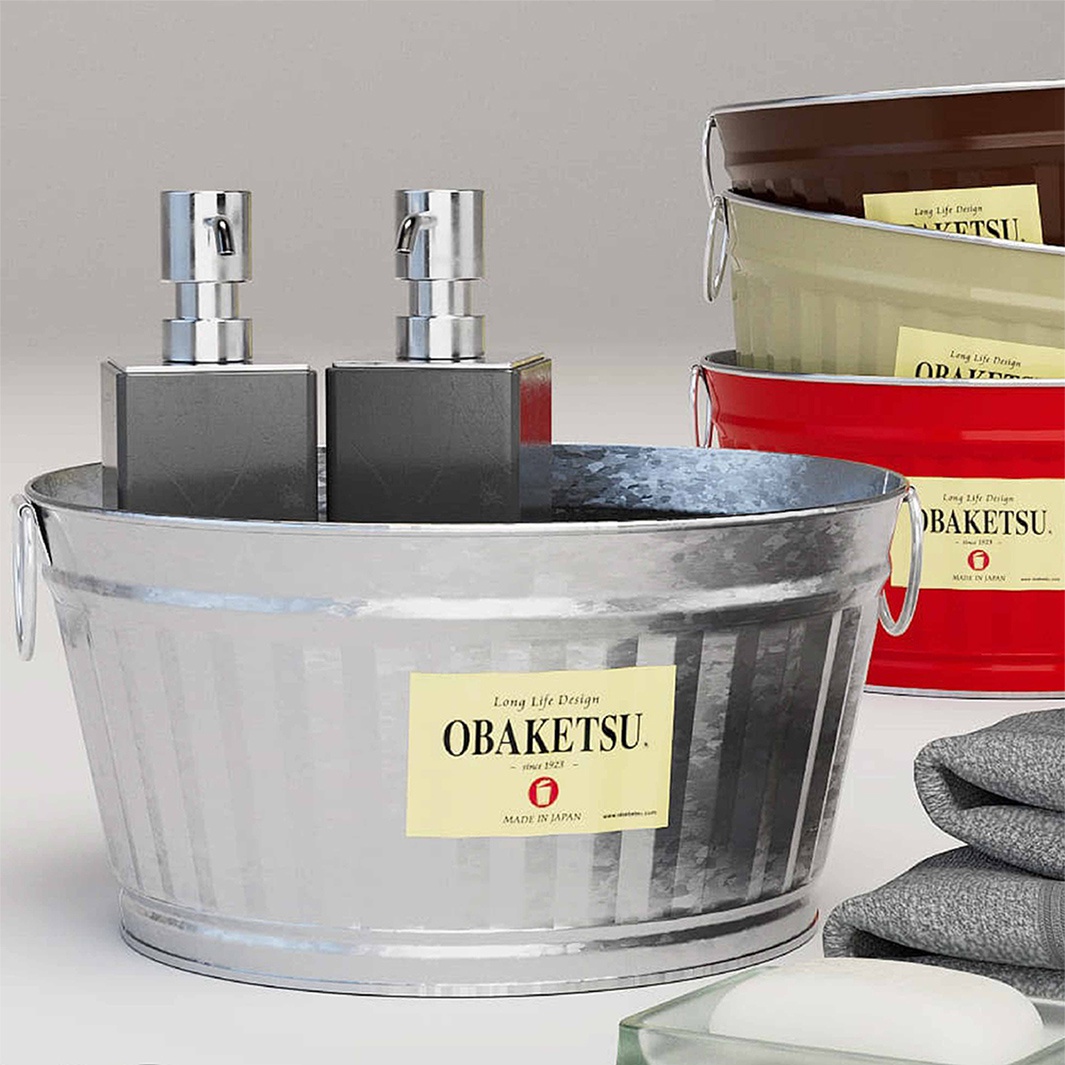 OBAKETSU 品牌的水桶，裡面擺放著兩個灰色皂液器，後方堆疊著不同顏色的水桶，右側有疊放的毛巾和一個透明皂盤，整體為浴室場景。