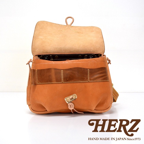 職人手作皮革鹿角扣繩郵差包，採用天然皮革製成，呈現溫潤的棕褐色。包身設計簡約，帶有可調節的繩索和鹿角造型的皮革扣環，風格獨特。包蓋內側有品牌標誌。