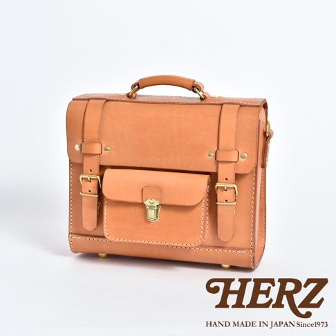 職人手作皮革學院風三用迷你後背包，採用天然皮革材質，呈現溫潤的淺棕色。包款設計有翻蓋式前袋、金屬鎖扣、可調式皮帶和扣環，另有頂部提把，整體風格簡約復古。