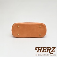 淺棕色皮革貝殼手提包底部，設有四顆金色金屬腳釘，包身以白色縫線裝飾。