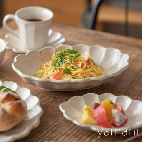 六魯粉引花型橢圓料理盤，以白色陶瓷製成，盤緣呈現花瓣狀，盤中盛有義大利麵，旁邊擺放著咖啡杯、麵包和水果盤。