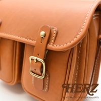 日本HERZ職人手作駝色皮革雙扣郵差包，特寫展示包包的縫線細節、金屬釦環與皮質的質感。