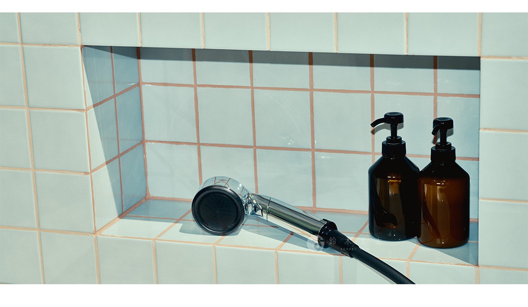 掛在藍色格子瓷磚壁龕中的金屬蓮蓬頭，旁邊擺放著兩個琥珀色泵頭分裝瓶。