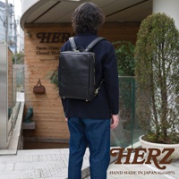 一名男子背著黑色軟皮商務後背包，後背包採用方形設計，配有金色拉鍊和可調節肩帶。