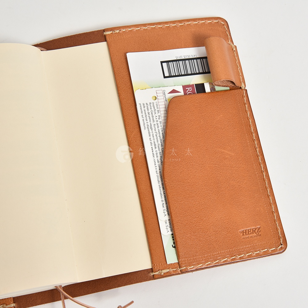 棕色皮革手帳書套，內有卡槽，左側為空白筆記頁，右側皮革內嵌有品牌標誌。