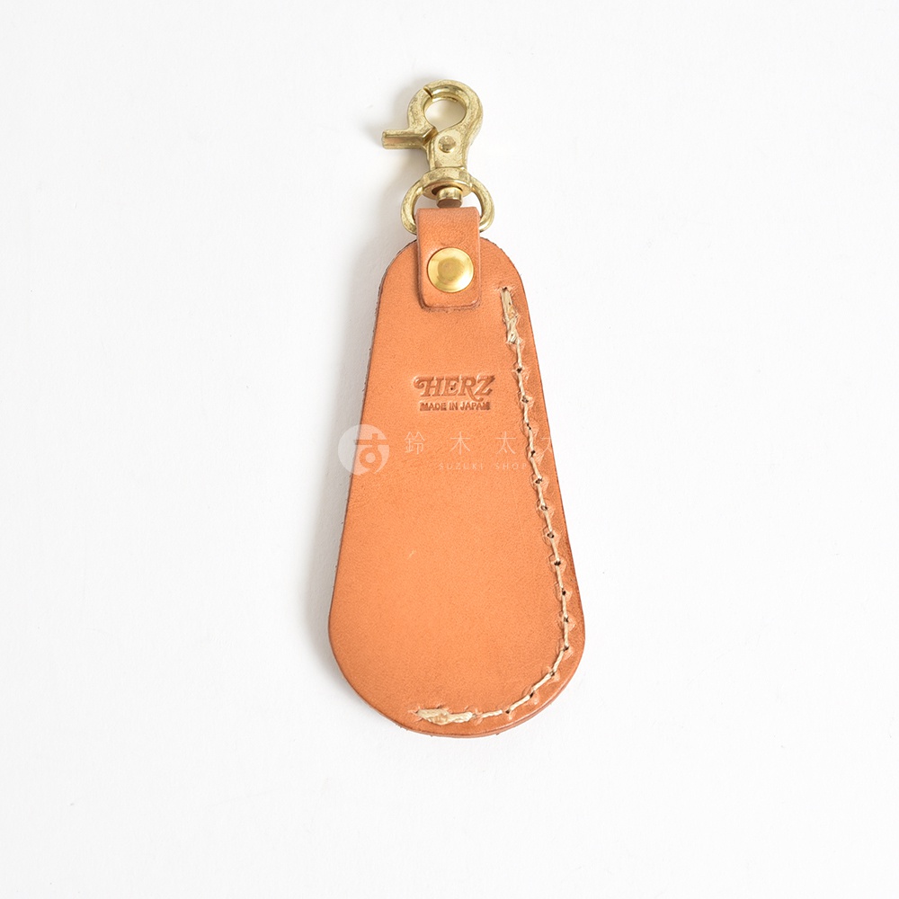 職人手作皮革隨身金屬鞋拔，淺棕色皮革，帶有金色金屬扣環及品牌壓印，縫線清晰，設計簡約。