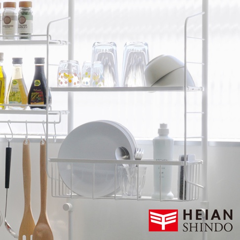 白色三層收納架，架上擺放有調味料瓶、玻璃杯、盤子、碗、餐具及清潔用品，架子上方還有掛鉤。