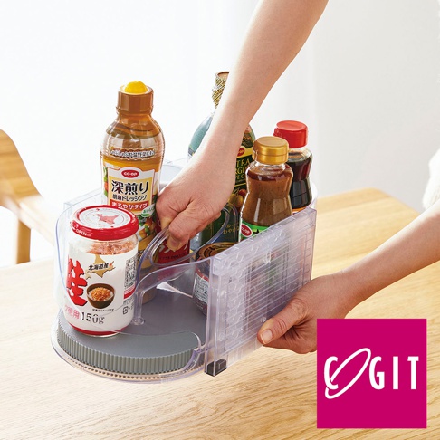 透明塑料製的多功能橢圓旋轉調味收納盤，盤內裝有數瓶不同醬料和調味品，例如日式醬油、芝麻醬等，盤底為灰色旋轉底座，由兩隻手操作。