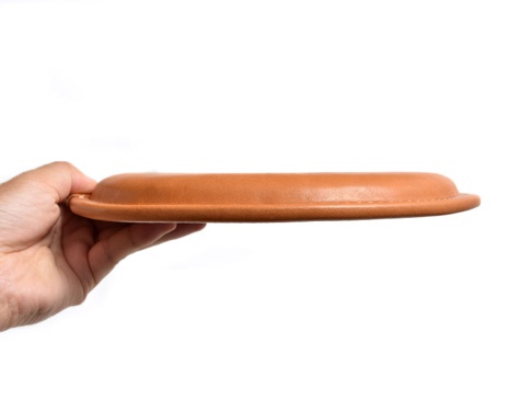 手持一個淺棕色皮革方形坐墊，展示其圓潤邊緣及車縫細節。