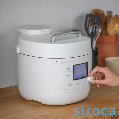 白色智能電子萬用壓力鍋，配有銀色提把和觸控螢幕，螢幕顯示日文菜單選項，操作旋鈕由一隻手轉動。