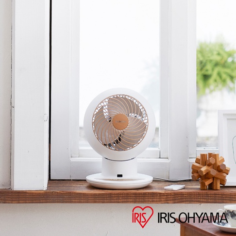 白色圓形空氣循環扇，扇葉及扇網格為木紋設計，置於木製窗台上，背景為模糊的窗外綠意。