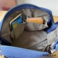 藍色石洗帆布旅行側背包內部，裝有手機和橘色零錢包，側邊有收納口袋。