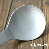 銀色鋁製湯勺，勺面帶有錘目紋理，勺柄修長，置於木製背景上。