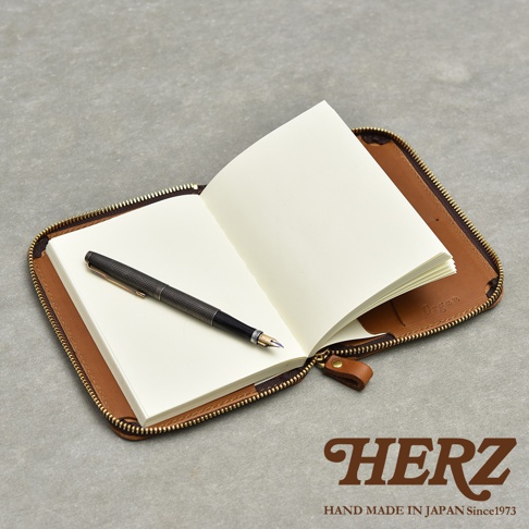 一個開放的棕色皮革記事本收納包，裡面放著一本空白筆記本和一支鋼筆。