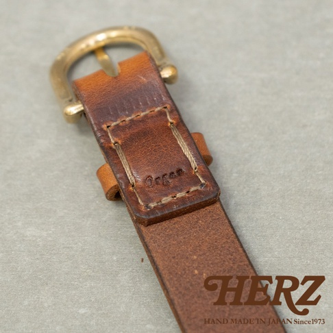 日本HERZ職人手作皮革Organ英倫皮帶，露出皮帶的金屬扣環和皮革細節，皮革上壓印有「Organ」字樣，右下角有「HERZ HAND MADE IN JAPAN Since1973」的文字。
