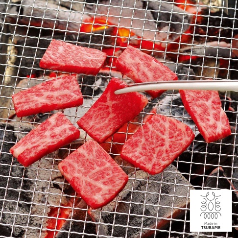 不沾桌公筷夾/餐夾，銀色金屬材質，夾著烤肉片，置於烤網上，網下有炭火。