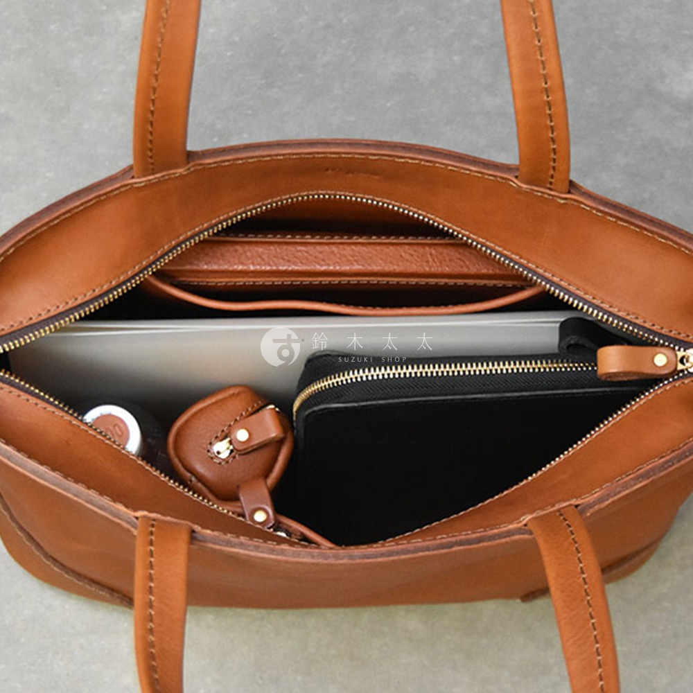 職人手作皮革Organ肩背拉鍊托特包，棕色皮革，內部裝有一個筆記型電腦、一個黑色拉鍊包和一個小皮革掛飾，包身設計簡約實用。