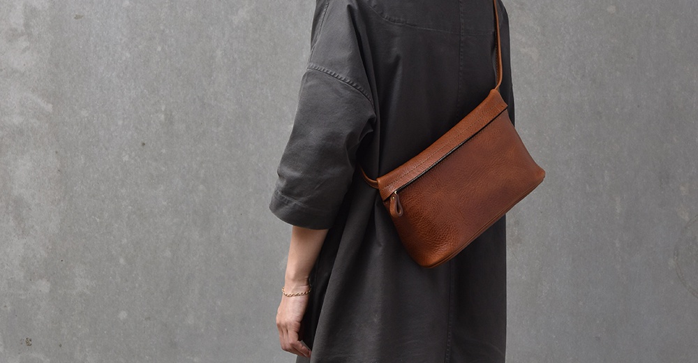 一位女士穿著深灰色寬鬆上衣，側背一個棕色皮革製的貼身斜背包，包包表面紋理清晰。