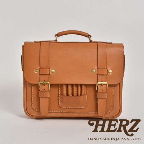 職人手作皮革傳統歐風三用學生包，淺棕色皮革，配有黃銅釦環和縫線，外層有一個附有筆插口袋，整體呈現復古風格。
