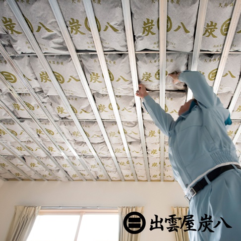 天花板結構上層層堆疊著印有金色「炭八」字樣的灰色調濕木炭包，由金屬支架固定。
