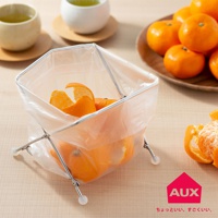 銀色金屬骨架搭配透明塑膠內袋的折疊式垃圾架，內含橘子皮與橘子，左側有兩個茶杯，右側有木盤裝著橘子。