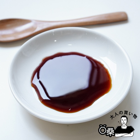 白色陶瓷小碟中盛有深褐色濃稠醬汁，醬汁表面光滑，反射出光澤。碟子後方有一支木質湯匙。