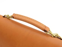 職人手作皮革雙扣兩用側背包 (CW-137) S，特寫近拍，展示了包包的提把細節。提把為淺棕色皮革材質，以縫線工藝製作，兩端連接黃銅色金屬掛鉤，可扣於包包兩側。