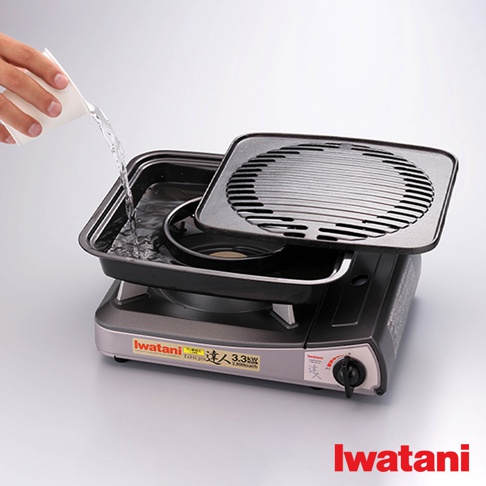 Iwatani 卡式爐上放置著一個黑色鑄鐵烤盤，烤盤內裝有水，其上疊放著帶有條狀紋路的烤網。烤盤與烤網均為黑色，材質為鑄鐵。