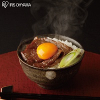 碗中盛著白米飯，鋪上香煎的牛肉片，中間放著一顆金黃的生蛋黃，旁邊點綴蔥段，散發著熱氣。