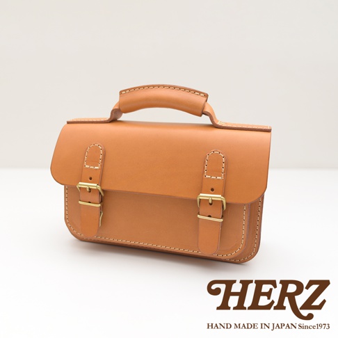 職人手作皮革雙扣兩用迷你肩背包，呈現溫潤的焦糖色皮革，搭配金色雙扣設計，簡約實用。