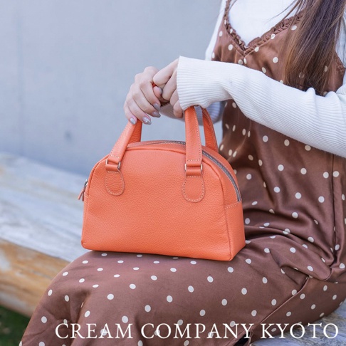 京都職人手作半月迷你手提包，採用橙色皮革，帶有圓潤的半月形輪廓，頂部設有雙提把與拉鍊開合。