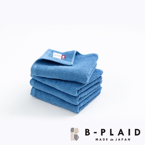 藍色今治毛巾疊放，表面有細小的鱗紋織紋，右上角有 B-PLAID 品牌標籤。