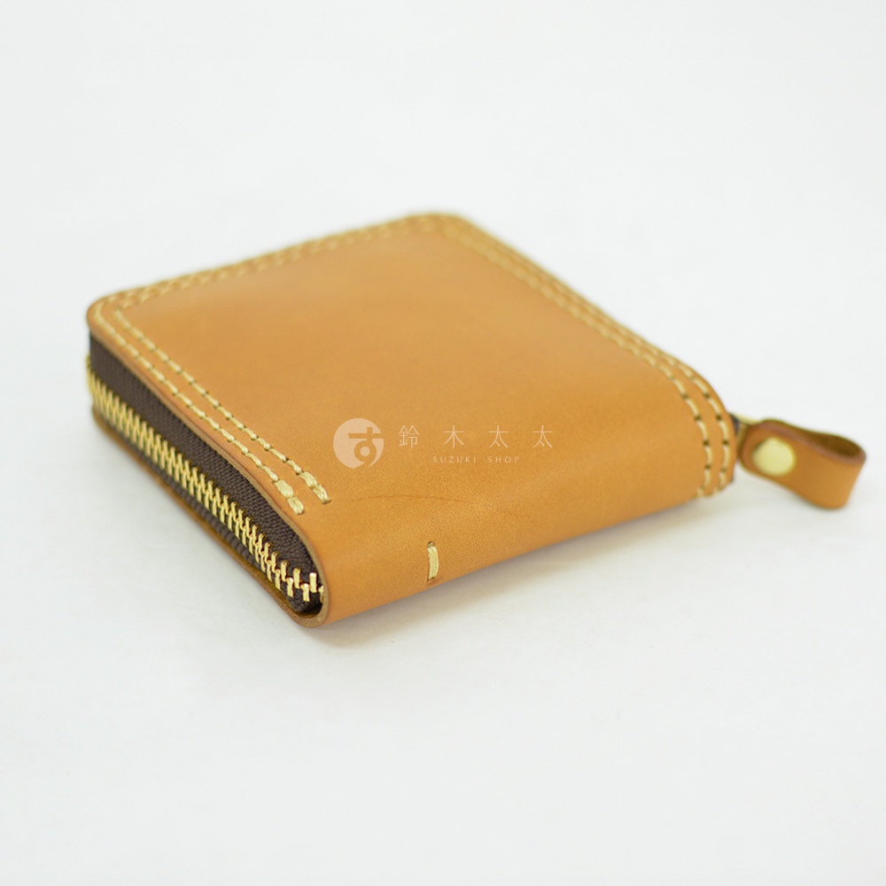 一個以淺褐色Latigo軟皮革製成的日本HERZ職人手作短夾，採用全包式拉鍊設計，邊緣飾有精緻的淺色縫線，右側配有金屬扣環的拉鍊頭，展現簡約質樸的皮革工藝質感。