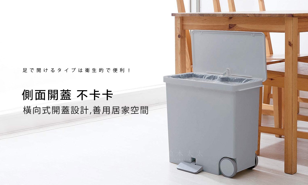 灰色寬型腳踏式分類垃圾桶，配有兩個內桶，側面有腳踏板，底部有兩個輪子，上方蓋子打開，置於木桌下方。