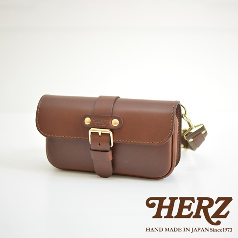 職人手作皮革單扣經典斜背包，採用棕色皮革製作，設有金色單扣和品牌標誌。