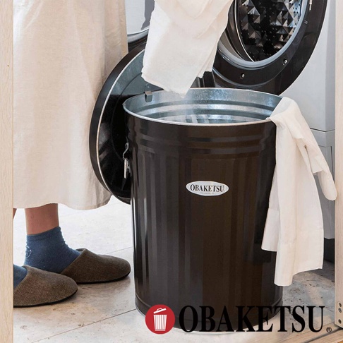 OBAKETSU 標誌的棕色金屬垃圾桶，人們正把白色的衣物丟進去。