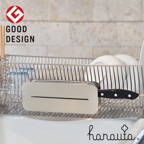 不鏽鋼臥式刀座，銀色，表面光滑，帶有細長切口，可插入刀具。刀柄為黑色，帶有白色鉚釘。刀座置於金屬置物架中，背景為淺色磚牆。