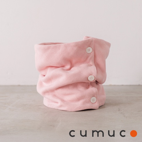 粉紅色 CUMUCO 八層紗舒適透氣保暖頸套，帶有三個白色鈕扣，在淺灰色紋理表面上，背景為白色牆壁。