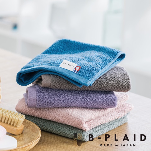 一疊五色（藍、灰、紫、粉紅、綠）今治毛巾，表面有鱗紋織法，頂部藍色毛巾帶有 B-PLAID 品牌標籤。