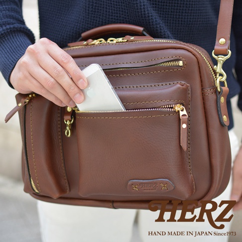 職人手作皮革兩用多功能收納單肩包，咖啡色牛皮材質，設有金色拉鍊和多個收納隔層，可斜挎或手提。