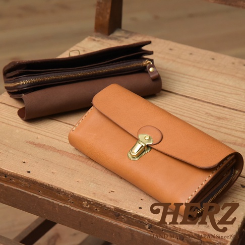職人手作皮革長夾，採用溫暖的淺棕色皮革，搭配金色鎖扣。手風琴式設計，多卡層隔間，展現精緻工藝。另一側為深棕色皮革長夾，拉鍊開合。