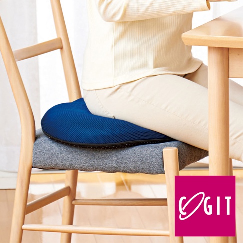 深藍色網狀蜂巢式冷凝膠坐墊，置於灰色布套坐墊上，坐墊置於木製餐椅上，一位身穿米色上衣及褲子的女士坐於坐墊上。