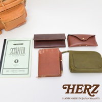 皮革製品組合，包含一個棕褐色皮製筆記本、一支筆、一個深棕色皮夾、一個紅褐色皮製筆盒，以及一個軍綠色皮製收納包。