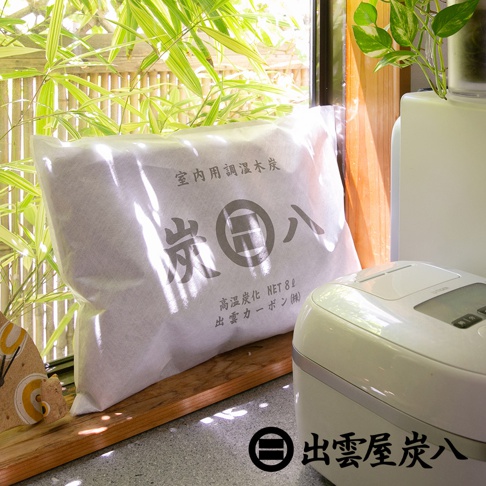 白色包裝袋裝著中大型室內調濕木炭，袋上印有灰色文字「炭八」及日文說明。旁邊是白色電飯鍋，背景為竹子與綠葉。