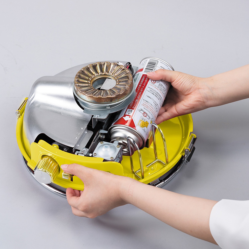 黃色卡式瓦斯暖爐，頂部有金屬燃燒器，側面有銀色旋鈕，正在安裝瓦斯罐。